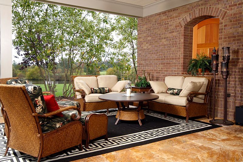 Outdoor seating area with wicker furniture, brick wall, and view of trees and lake.