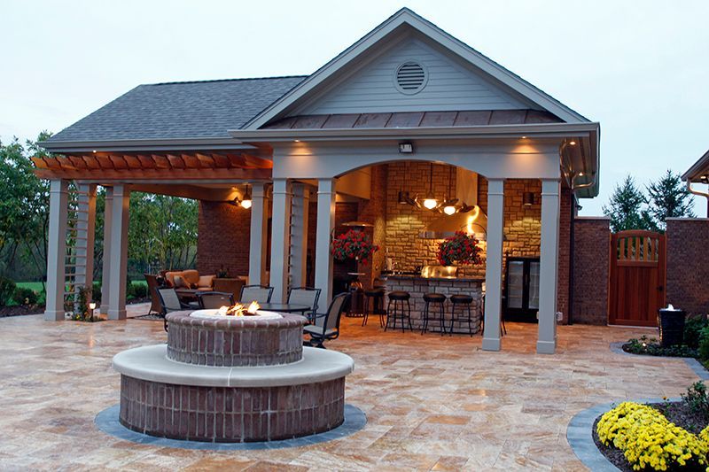 Outdoor patio with a fire pit, bar, and seating under a covered structure with brick accents.