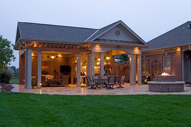 Outdoor patio with seating, fireplace, brick columns, and a low brick fire pit, at dusk.