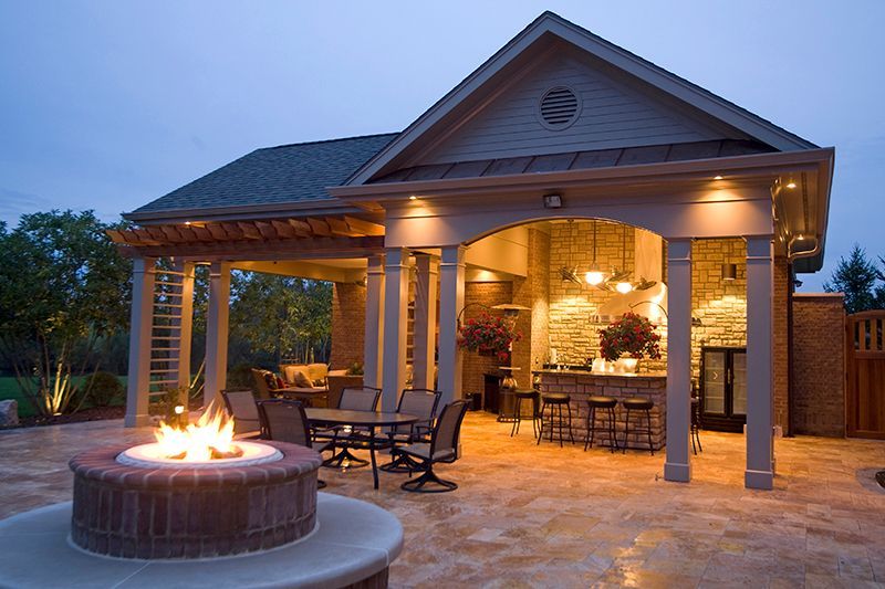 Outdoor patio with fire pit and bar, lit at dusk.