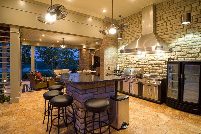 Outdoor kitchen with stone walls, granite countertop, stainless steel appliances, and bar seating.