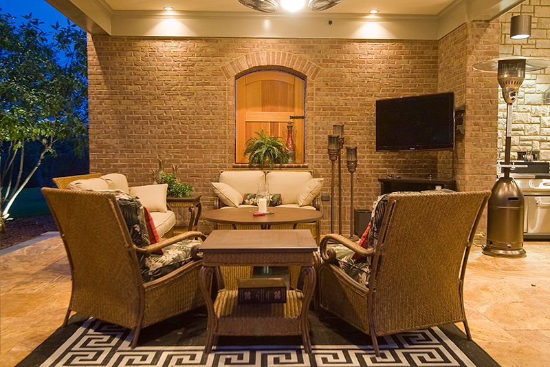 Outdoor seating area with wicker furniture, brick wall, and TV; illuminated at night.