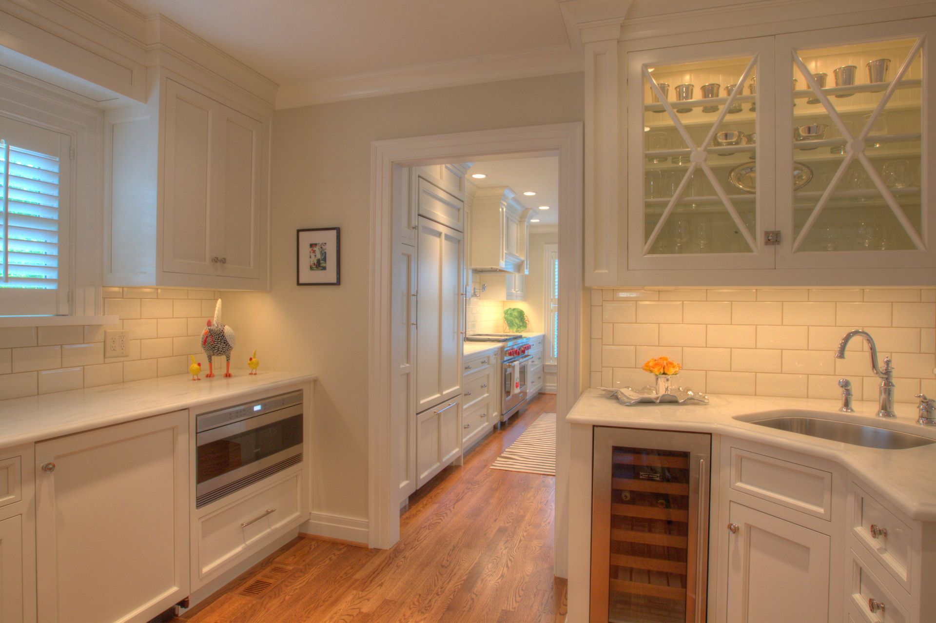White kitchen with built-in microwave, sink, and wine fridge; doorway leads to another kitchen area.