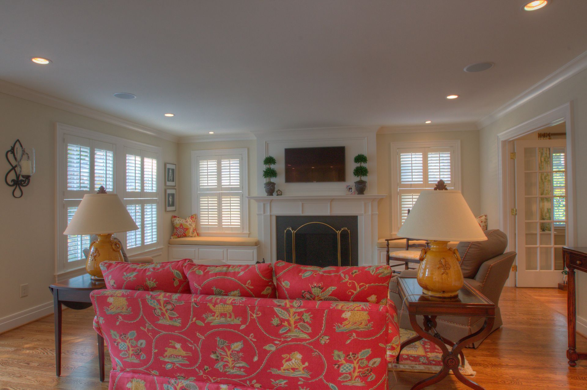 Living room with red floral sofa, fireplace, and shuttered windows.