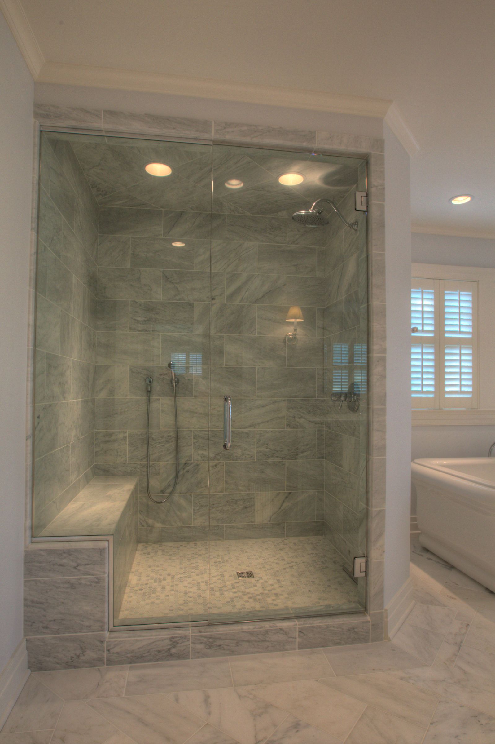 Glass shower with marble tile, bench, and fixtures in a light-filled bathroom.