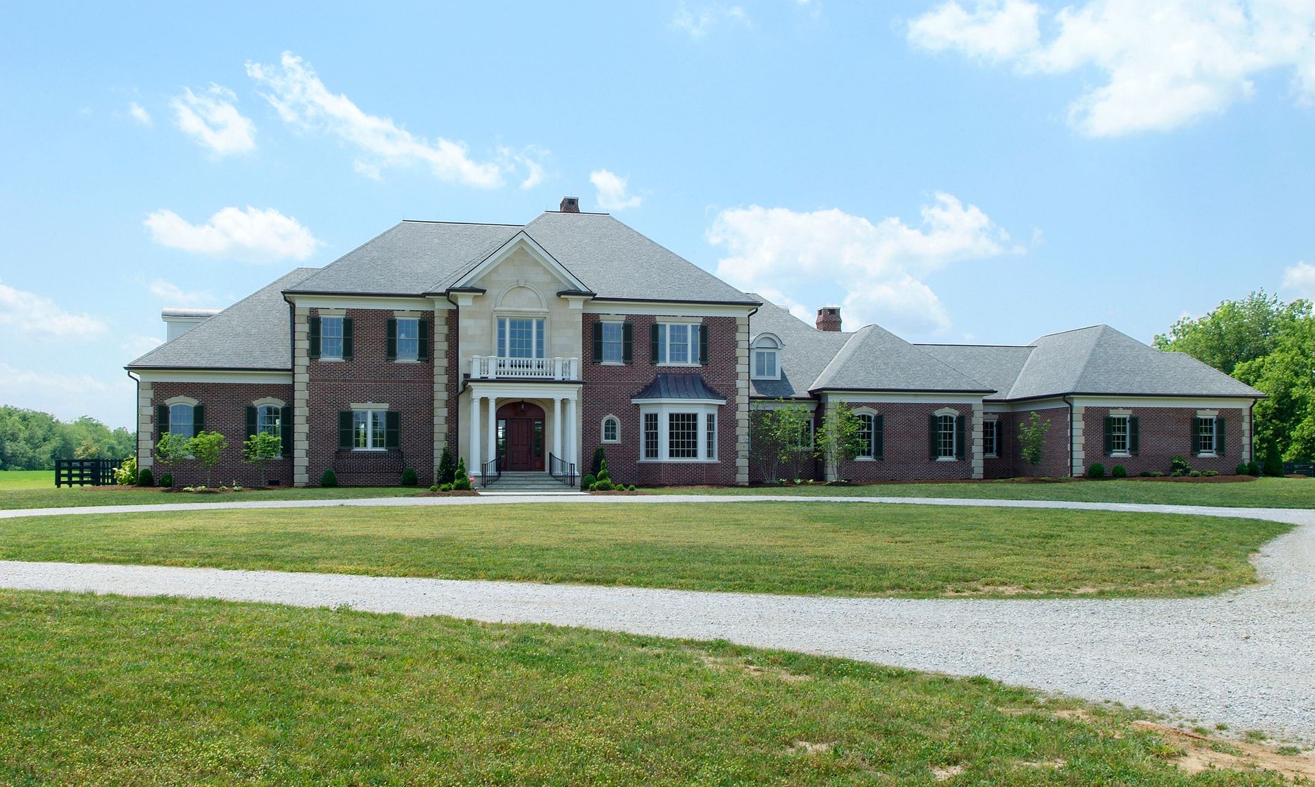 Large brick house with gray roof and green lawn, under a blue sky.
