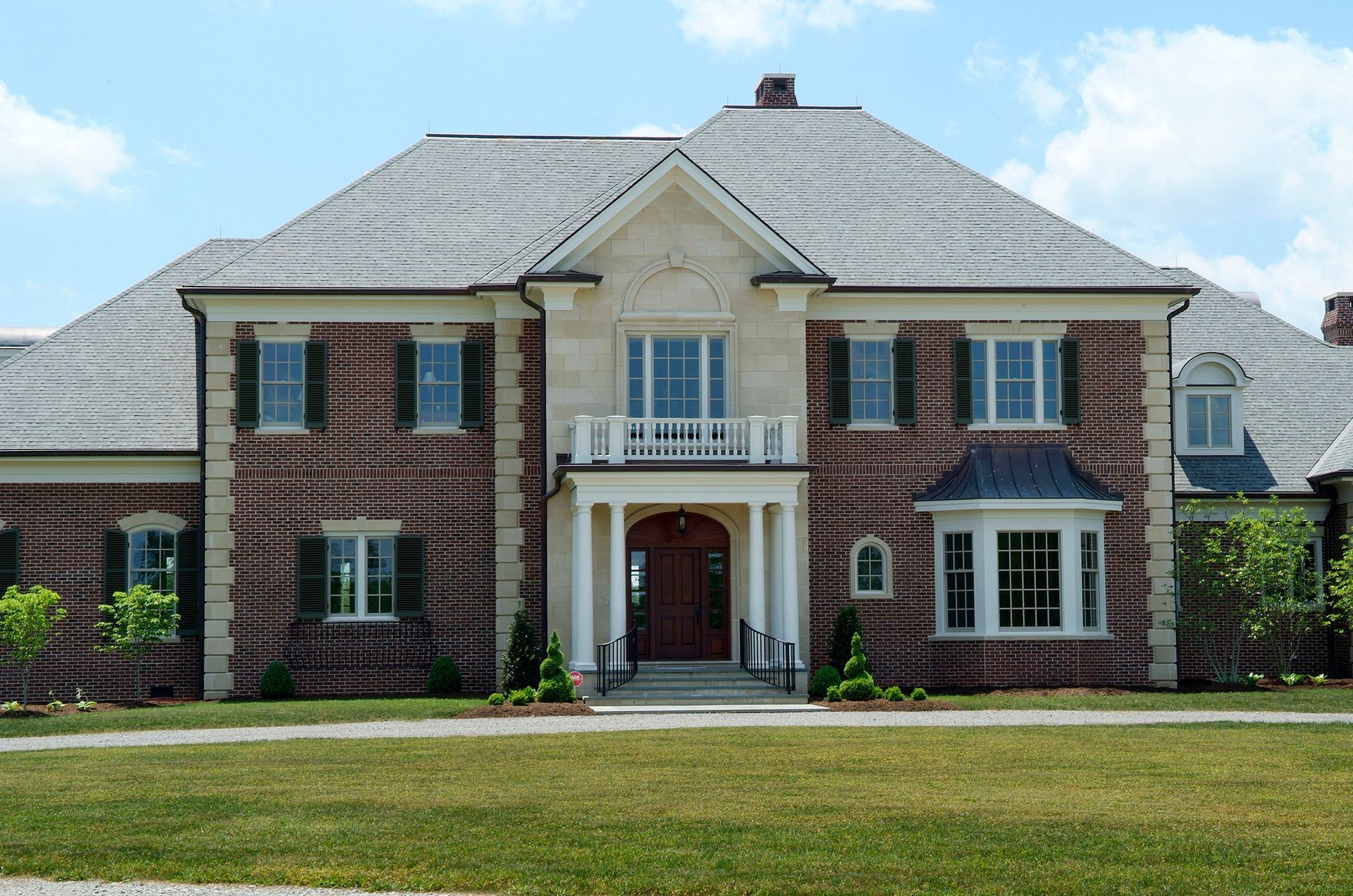 Two-story brick house with white trim, shutters, and a central balcony, under a blue sky.