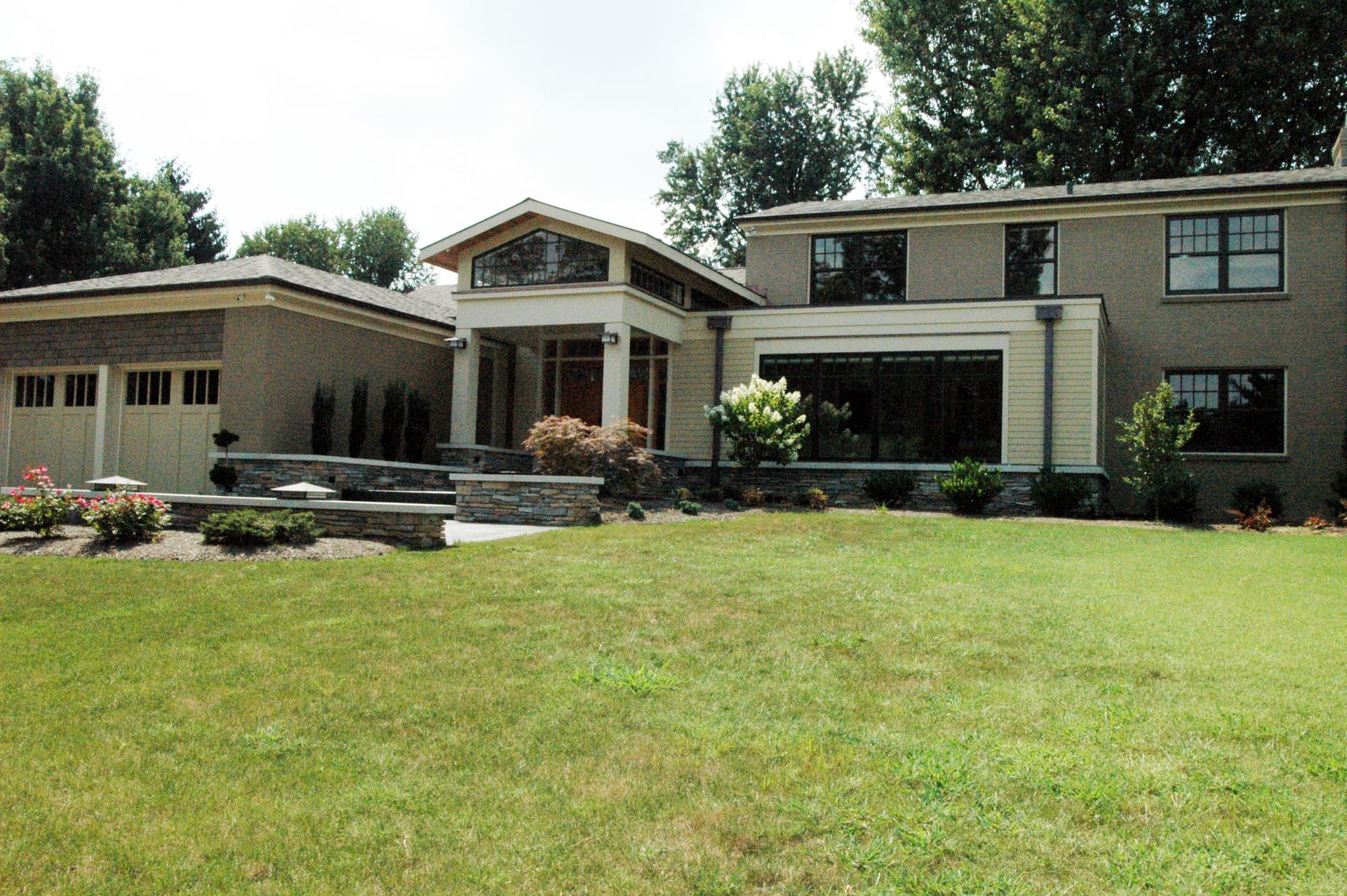 House with stone facade, green lawn, and garage. Blue sky, trees in background.