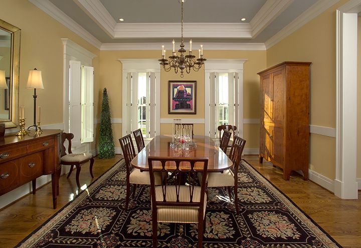 Formal dining room with a long wooden table, rug, chandelier, and a tall cabinet.