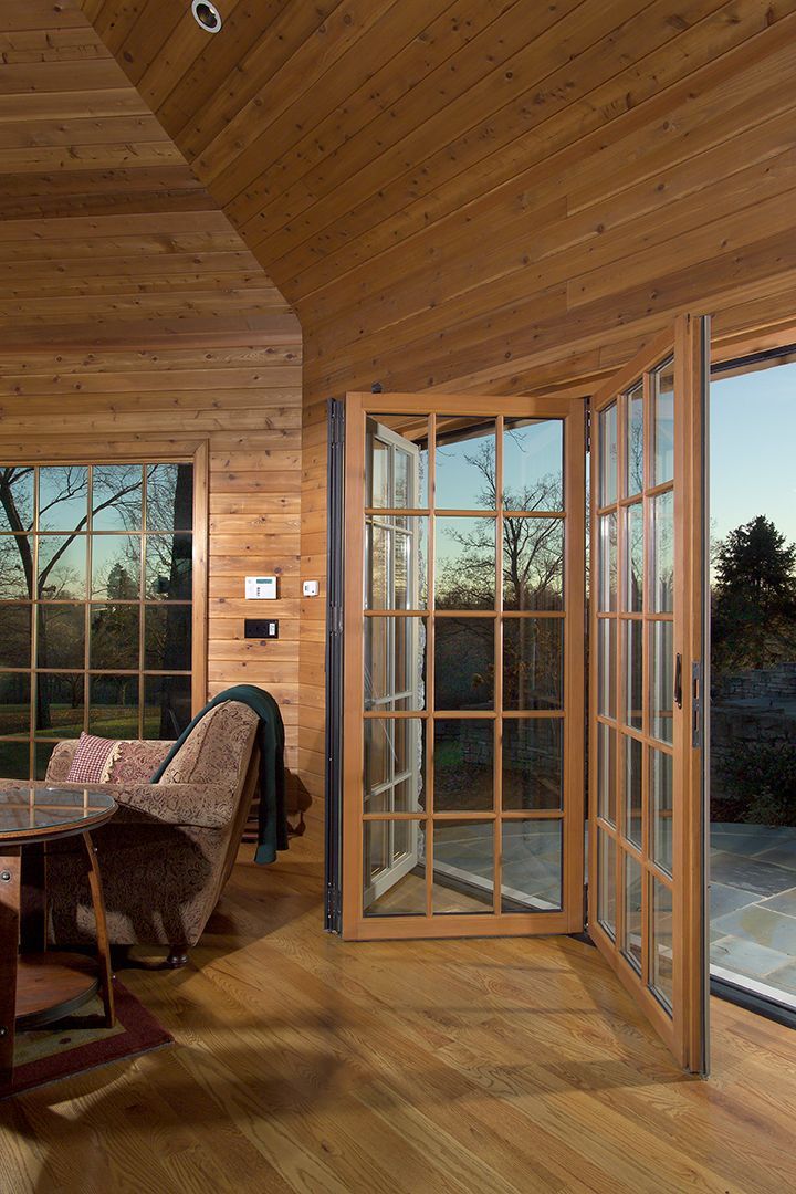 A wooden-paneled room with open French doors to a view of trees and an outdoor patio.