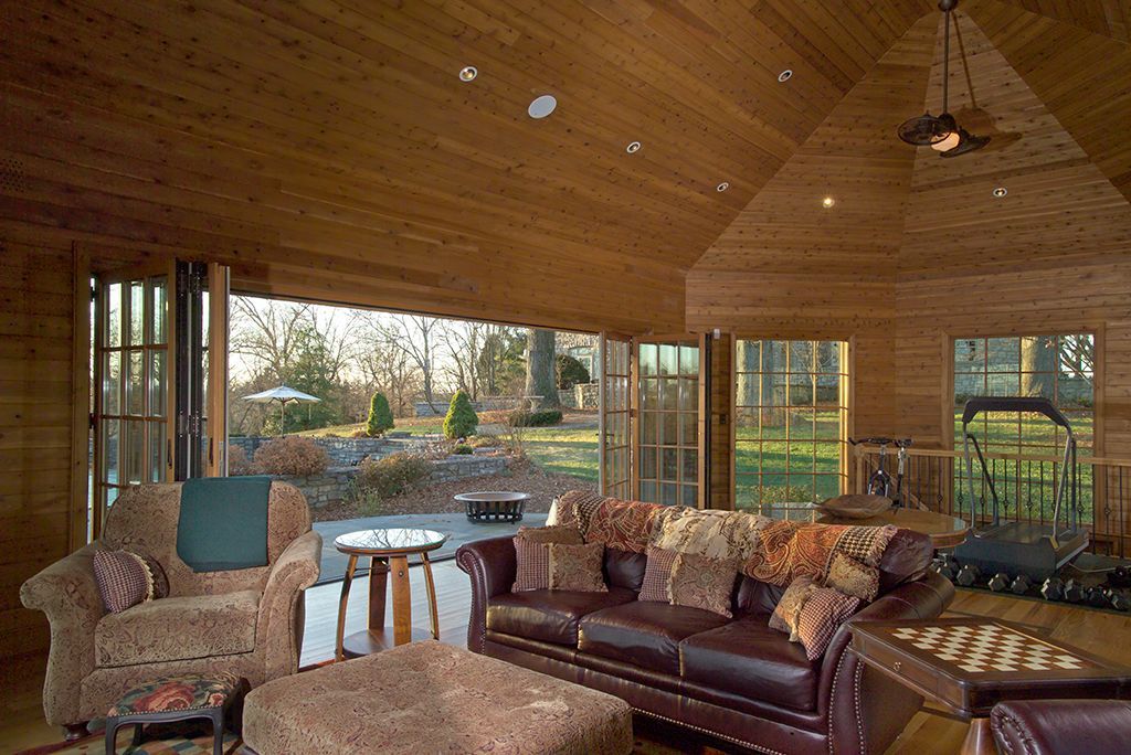 Wooden room with open doors leading to a patio. Brown leather furniture, a treadmill, and outdoor view.