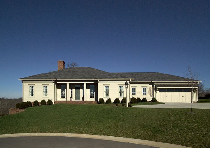 Tan ranch-style house on a grassy hill with a clear blue sky above.