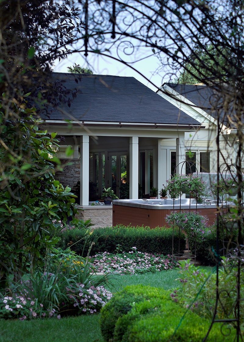 Garden with manicured lawn, stone wall, and house with covered patio framed by a decorative iron arch.