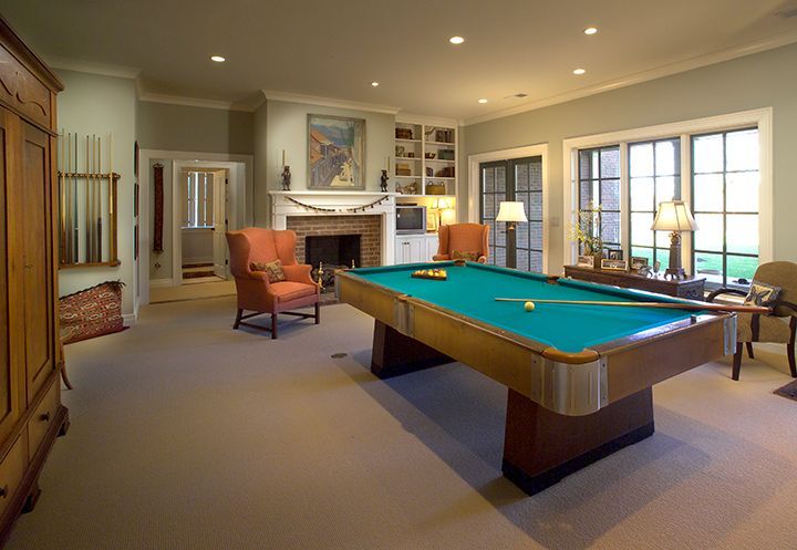 Pool table in a well-lit room with a fireplace, two armchairs, and a large window.
