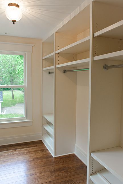 Built-in white closet with shelves, hanging rods, and wooden floor in a room with a window.