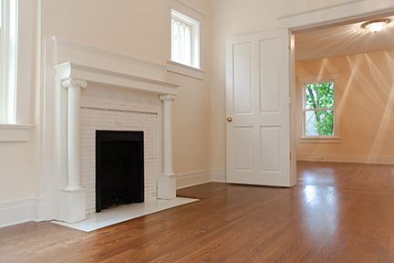 Empty room with fireplace, hardwood floors, and doorway to another room.