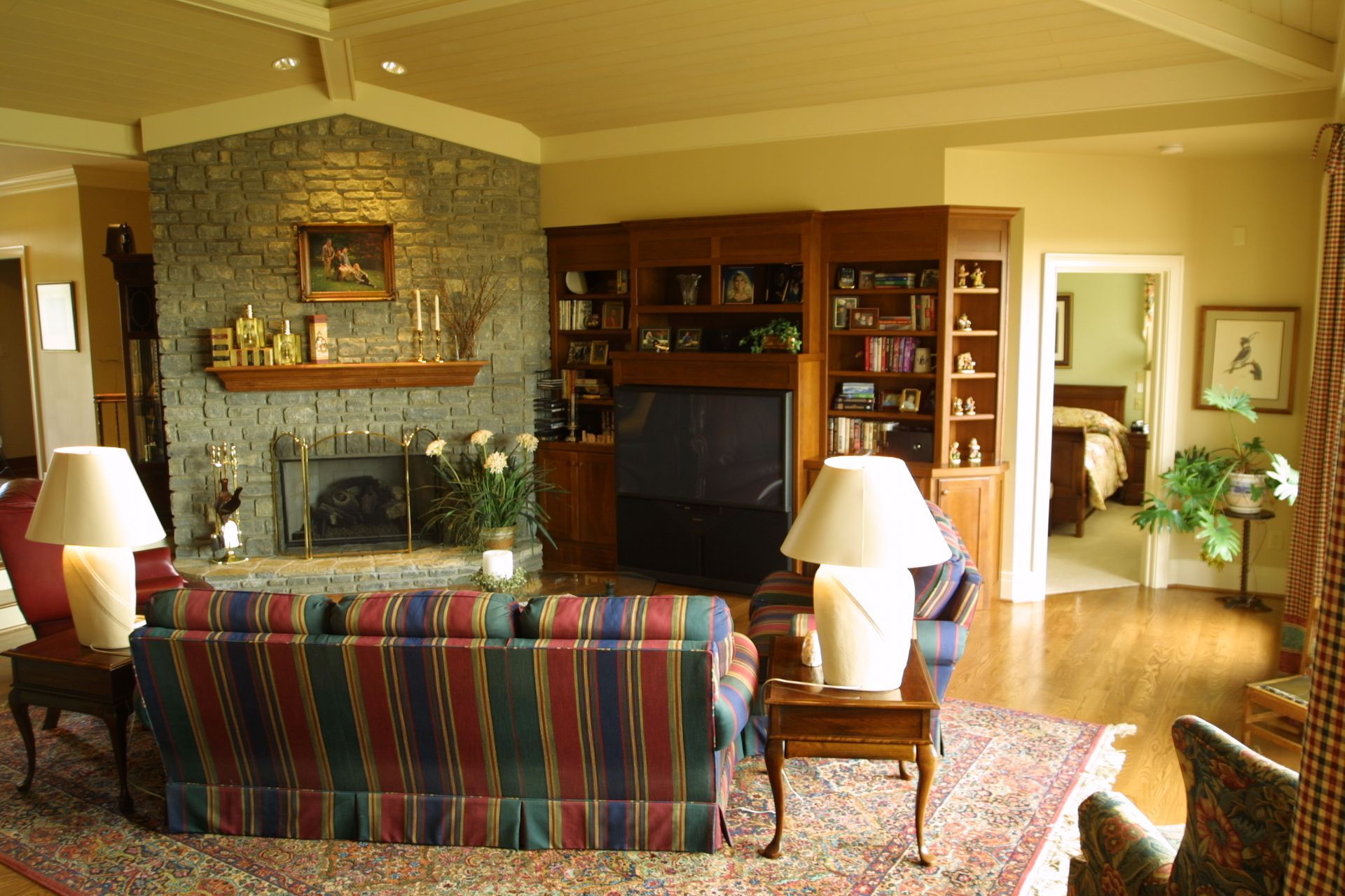 Cozy living room with stone fireplace, built-in media center, striped sofa, and lamps on side tables.