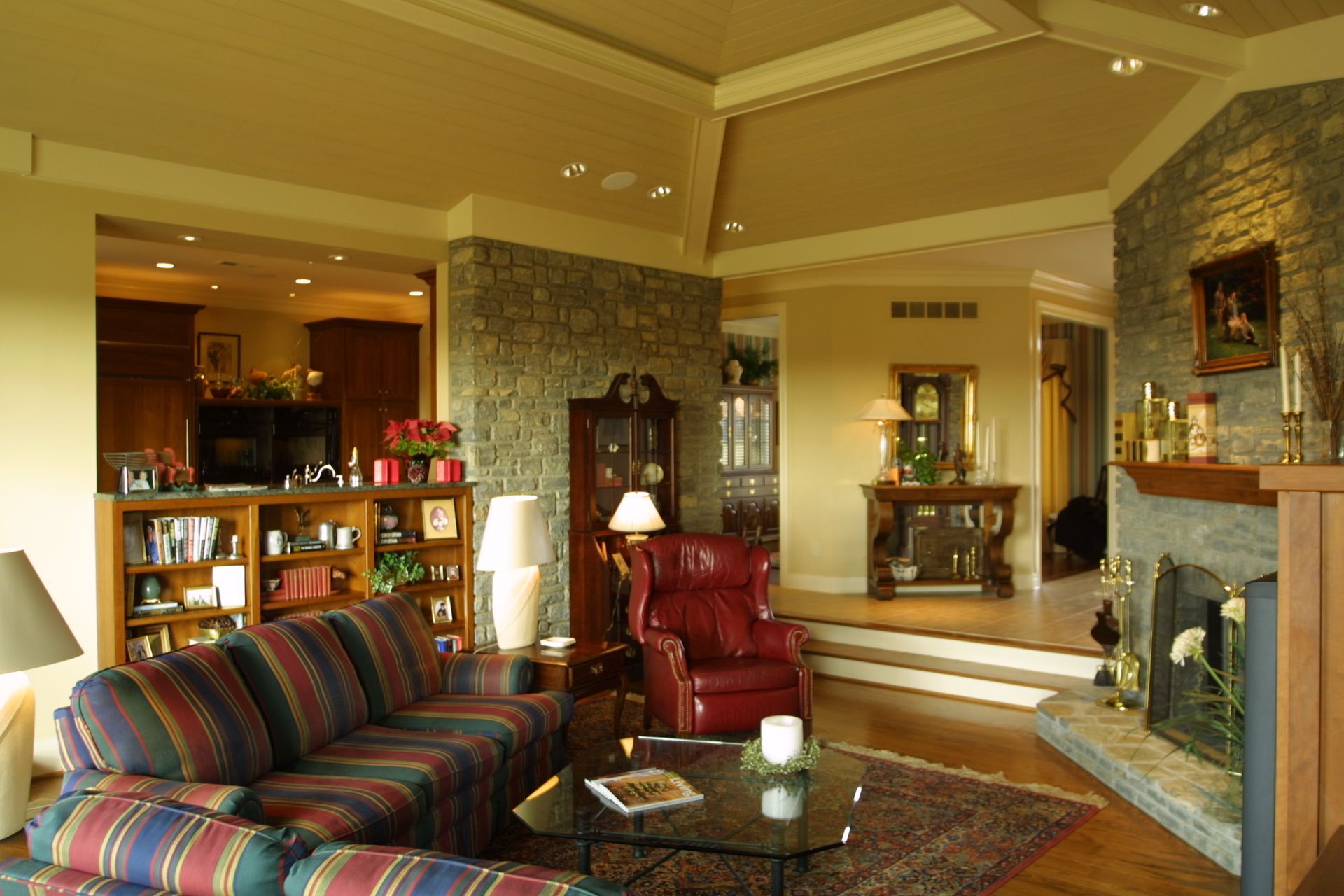 Living room with stone fireplace, red armchair, and a colorful striped sofa.