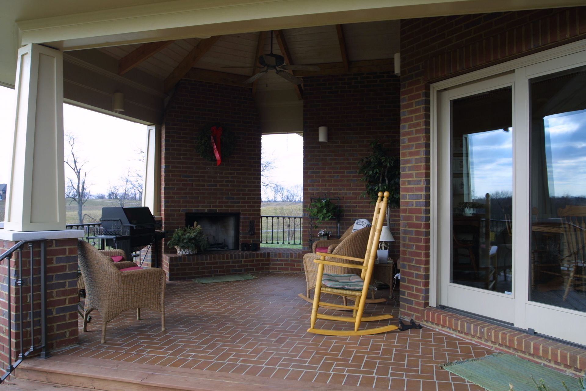 Covered brick patio with a fireplace, grill, and rocking chair.