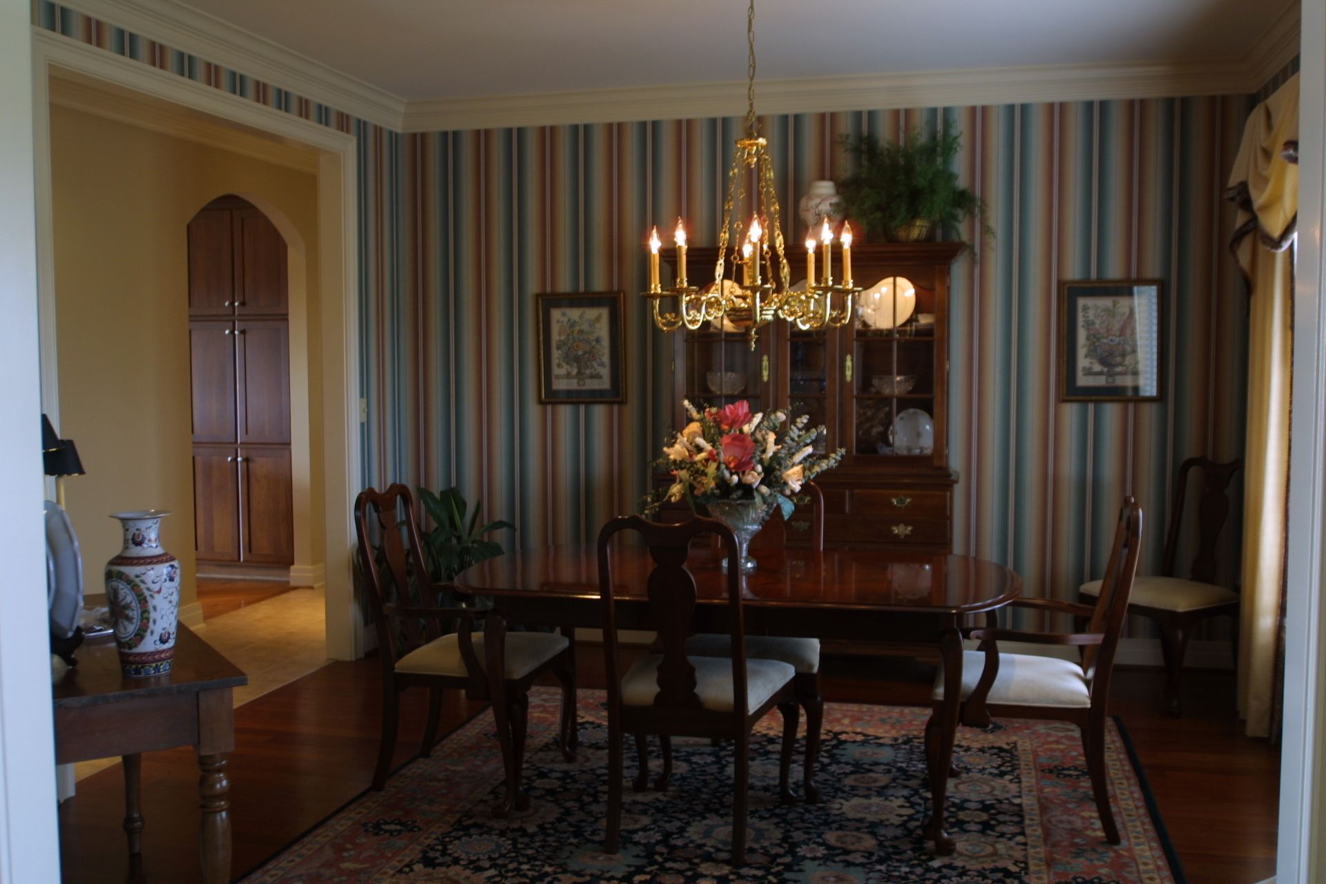 Dining room with striped wallpaper, chandelier, wooden furniture, and floral centerpiece.