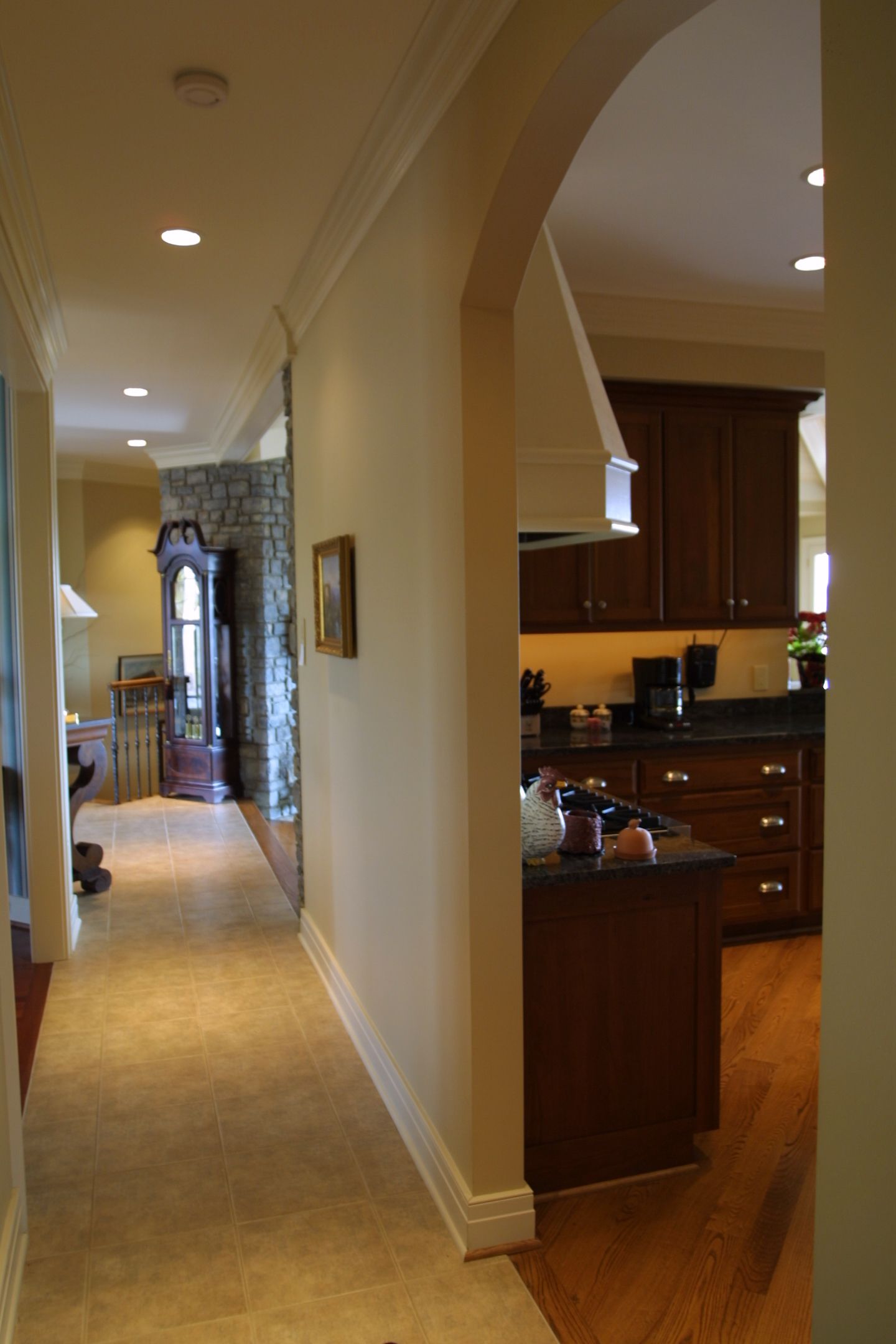 Hallway with archway leading to kitchen; cream walls, wood floors, recessed lighting.