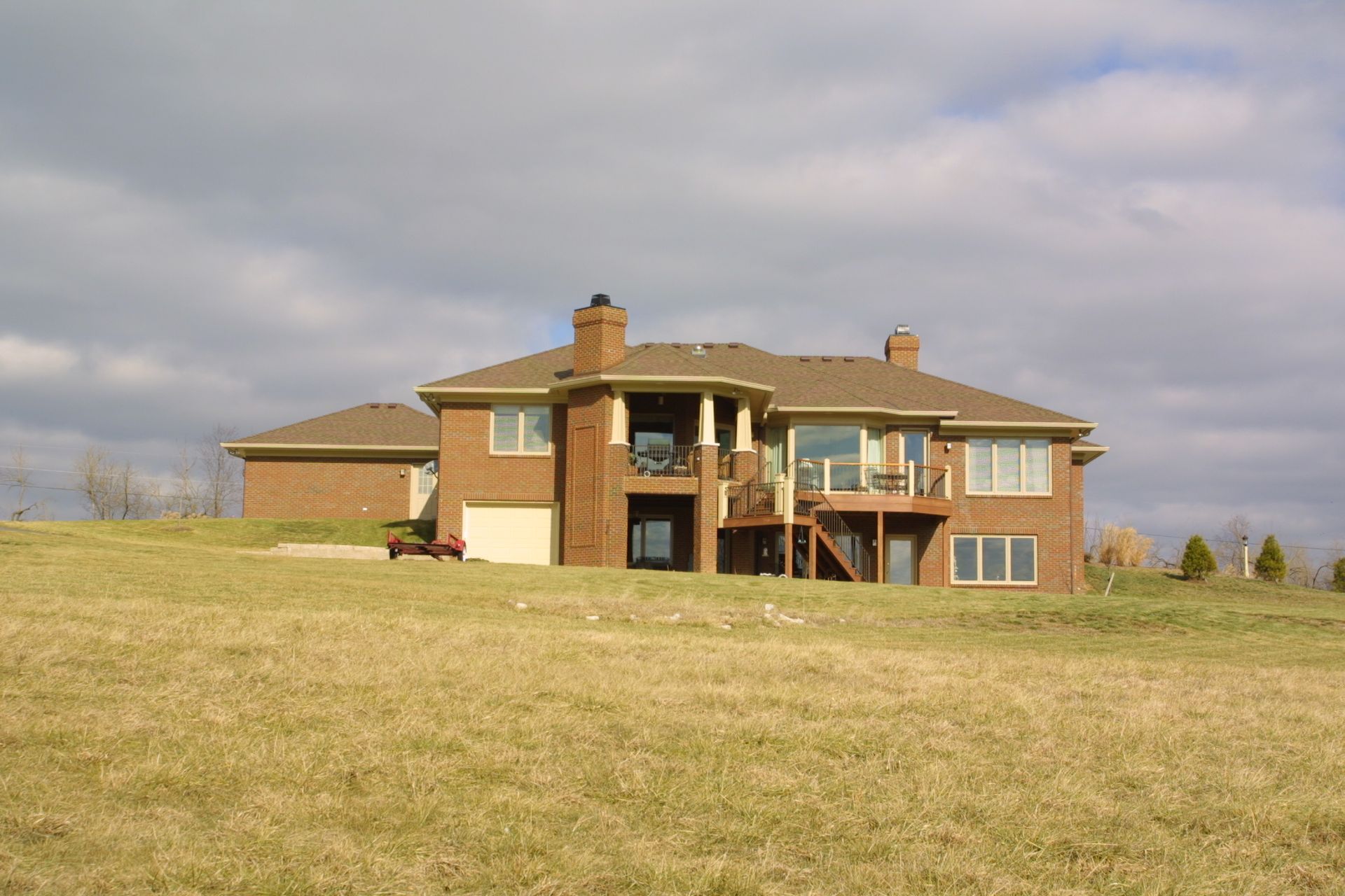 Brick house on a grassy hill under a cloudy sky.