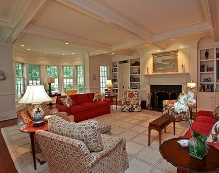 Living room with red and floral furniture, fireplace, built-in shelves, and a bay window.