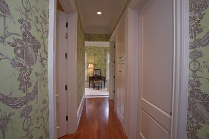Hallway with green patterned wallpaper, white doors, and wood floor leading to a furnished room.