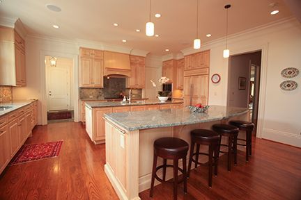 Spacious kitchen with light wood cabinets, granite countertops, island with bar stools, and hardwood floors.