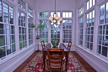 Dining room with many windows, wooden table, and red rug.