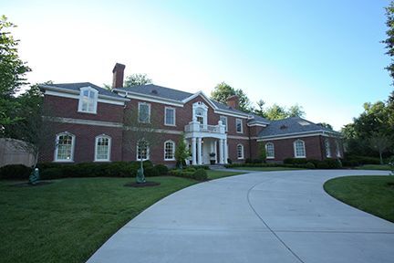 Large red brick mansion with white columns, long driveway, and green lawn.