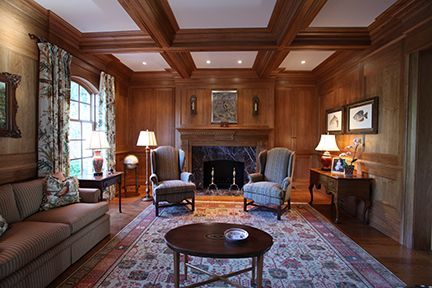 Cozy wood-paneled room with fireplace, two armchairs, sofa, area rug, and round coffee table.