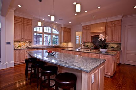 Spacious kitchen with light wood cabinets, two islands with granite countertops, and dark leather stools.
