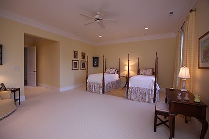 A spacious bedroom with two four-poster beds, a desk, and a sofa; light yellow walls and cream carpet.