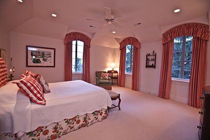 Spacious bedroom with white walls, arched windows, and a king-size bed with floral accents and red curtains.
