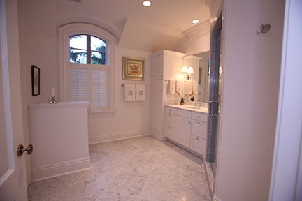 White bathroom with marble floors, arched window, white cabinetry, and a glass shower.