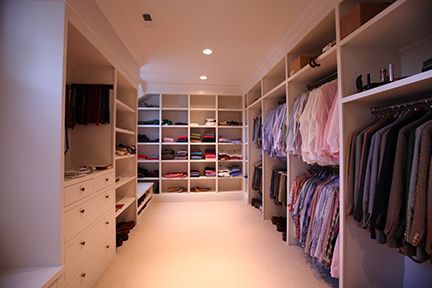 Walk-in closet with white shelves and drawers filled with clothing. Well-lit space with a neutral color scheme.
