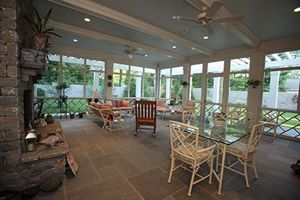 Spacious screened porch with fireplace, dining area, and seating. Stone floor, pale blue ceiling.