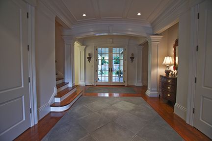 Elegant foyer with archway leading to French doors, steps on the left, and a dresser on the right.