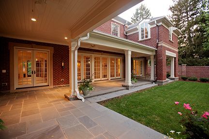 Brick house with covered patio, stone patio flooring, and green lawn.