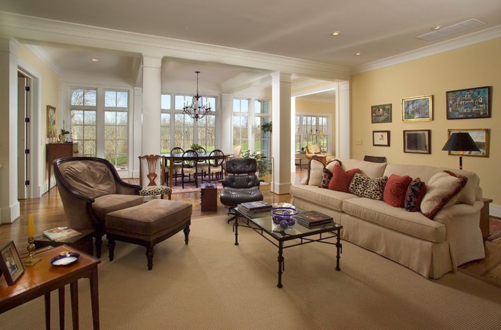 Living room with tan walls and furniture, open to dining room with chandelier and windows.