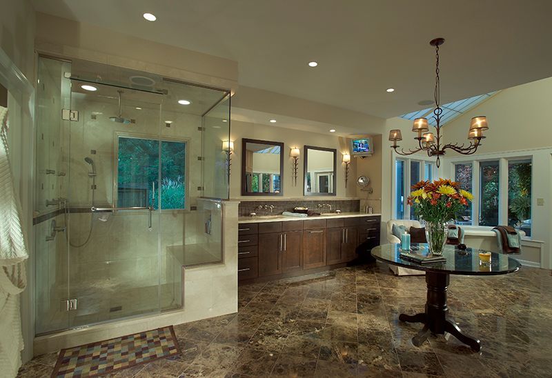 Spacious bathroom with glass shower, dark wood vanity, and marble floors. Table with flowers under a chandelier.