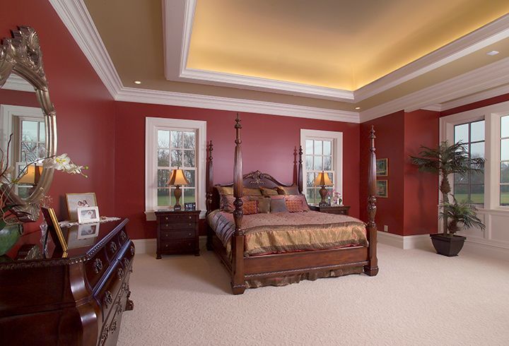 Red-walled bedroom with four-poster bed, nightstands, windows, and ceiling lights.