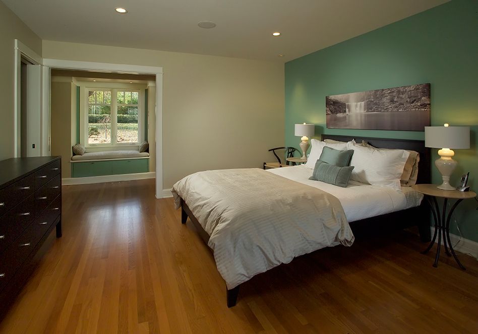 Bedroom with hardwood floors, a bed, and a window seat with green walls.