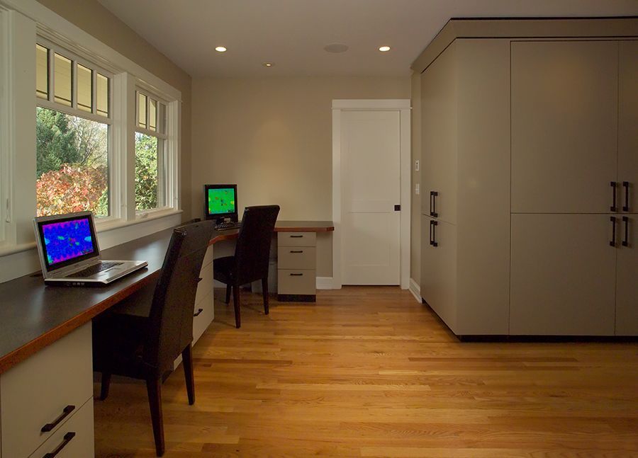 Home office with two desks by a window, cabinets, hardwood floor, and a door.