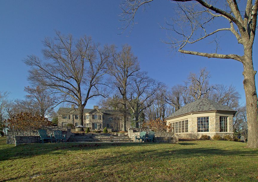 Lawn with stone buildings, bare trees, and blue chairs on a patio under a clear, sunny sky.