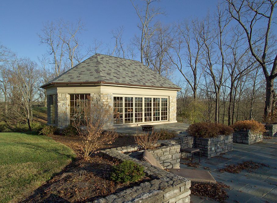 Stone building with windows, on a hillside patio. Gray roof, surrounding trees, sunny day.