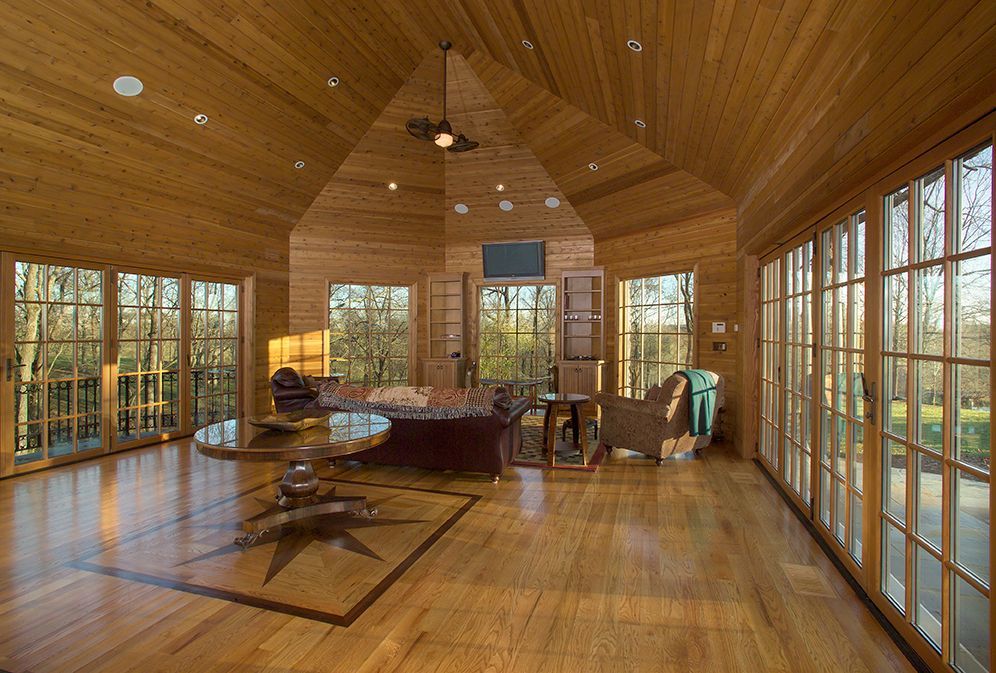 Wooden-paneled room with large windows, furniture, and a starburst design on the wooden floor.
