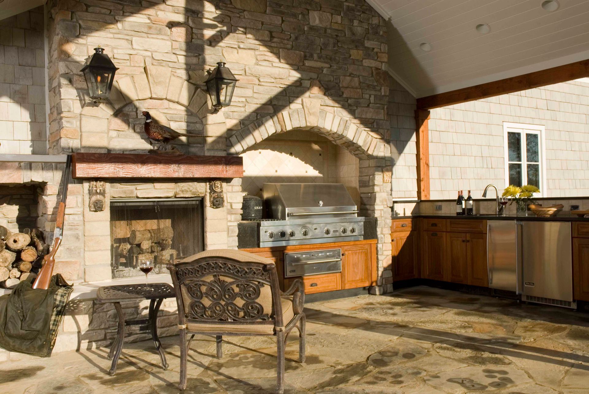Outdoor kitchen with stone walls, fireplace, grill, cabinets, and seating area.