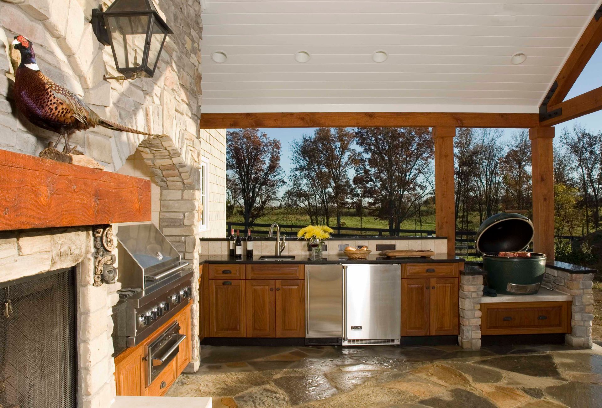 Outdoor kitchen with fireplace, grill, cabinetry, and Big Green Egg, with a scenic view.